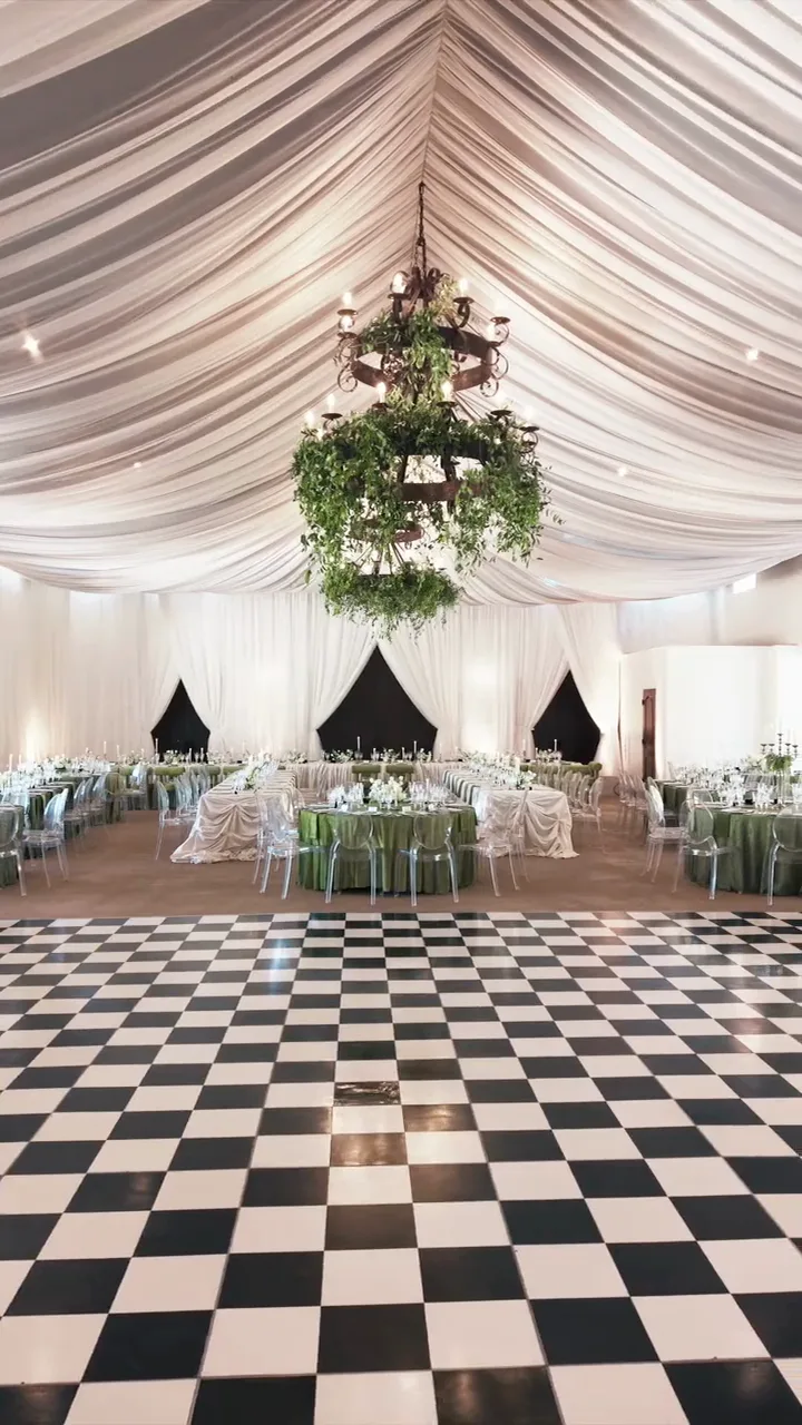 A tented reception with a chandelier over a checkerboard floor